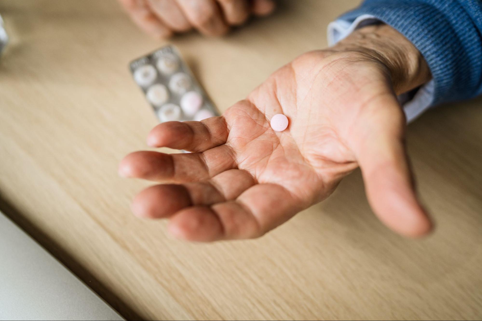 A hand holding a pill with a blister pack in the background